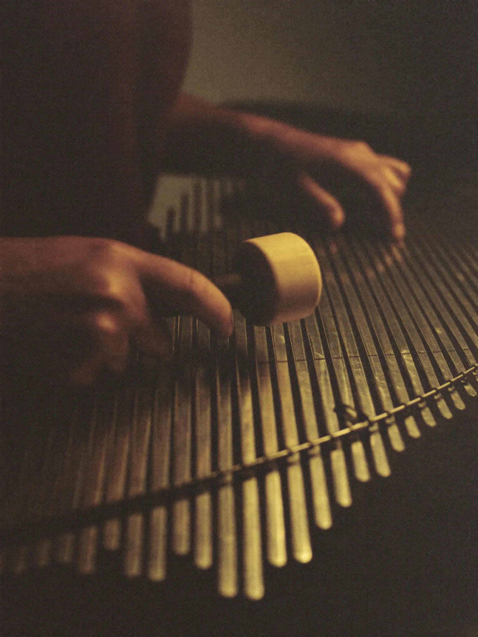 Hands playing a bronze saron gamelan instrument with a wooden mallet