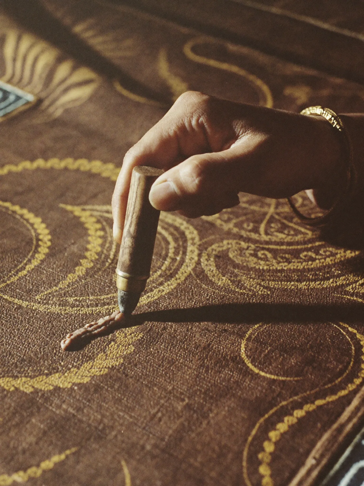 A hand applying hot wax with a canting tool onto batik cloth